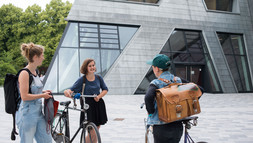 Studierende unterhalten sich mit Fahrrad vor dem Zentralgebäude